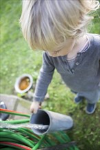 A little boy standing at a garden hose making water pass through a tube