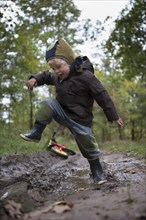 Little boy jumping with joy into a muddy puddle during an autumn walk