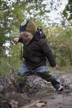 A little boy is jumping with joy into a muddy puddle during an autumn walk