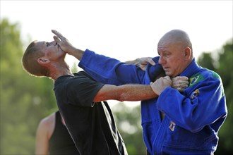 A martial arts instructor is demonstrating a defensive move on a student in a park