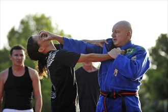 A martial arts instructor is showing a defensive move on a student in a park