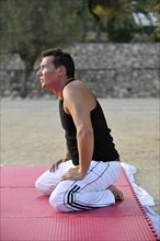 A martial arts student is kneeling on an exercise mat in a park