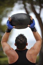Man holding a medicine ball over his head while exercising in a park