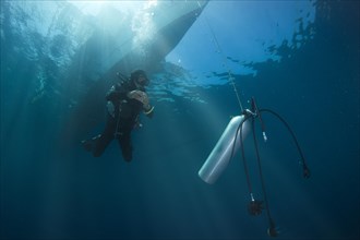 Diver with spare air tank during a decompression stop under a boat