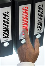 Hand pointing to a ring binder labelled "ABMAHNUNG"