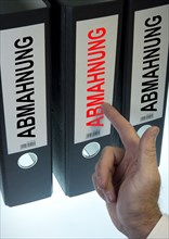 Hand pointing to a ring binder labelled 'ABMAHNUNG'