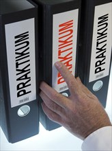 Hand reaching for a file folder labeled 'Praktikum'