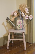 Antique watering can on top of a small chair in an old Canadiana cottage style wooden siding residential home