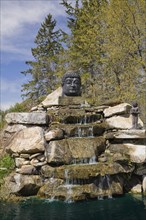 A large sculptured Budhead on top of the waterfall in the Zen garden at the 'Route des Gerbes d'Angelica' garden in Mirabel