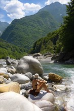 Young lady sunbathing by rocky alpine foothills stream in the remote valley of Val Verzasca