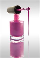 Pink nail varnish dripping from a nail varnish brush balanced on a nail varnish bottle
