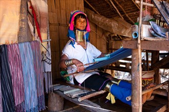 Long-necked Padaung woman wearing neck rings weaving a garment