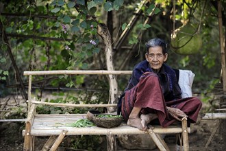 Elderly woman sitting on a bench made of bamboo