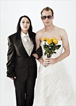 Bride wearing a suit and a groom wearing a wedding dress with sunglasses and yellow roses