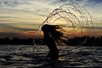 Young woman standing in the sea throwing back her long hair with splashing water