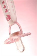 Pink pacifier hanging on a ribbon with a duck motif