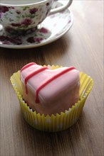 Pink heart-shaped petit four on a wooden surface beside a coffee cup