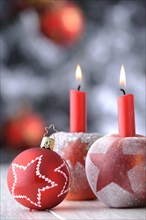 Red Christmas bauble with apples and candles in front of a Christmas tree