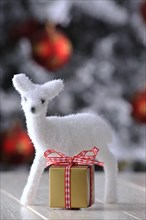 Figure of a white fawn with a golden gift in a Christmas ambience