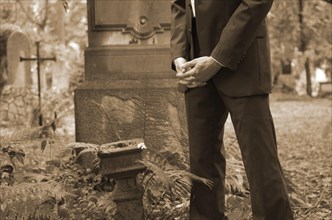 Man in a suit standing with folded hands at a gravesite