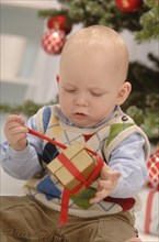 Toddler unwrapping a golden gift in front of a Christmas tree