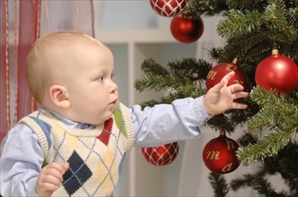 Toddler reaching for baubles on a Christmas tree