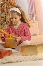 Girl unpacking a gift in front of a Christmas tree