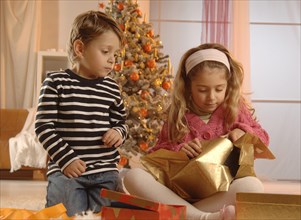 Girl and boy unpacking gifts in front of a Christmas tree