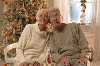 Mature couple with headphones sitting in front of a Christmas tree