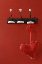 Red fabric heart hanging from nostalgic clothes hooks on a red wall