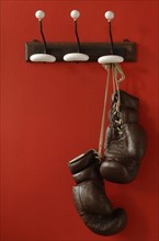 Boxing gloves hanging on nostalgic coat hooks on a red wall