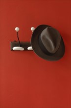A man's hat is hanging on nostalgic clothes hooks on a red wall
