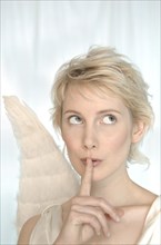 Blonde woman with angel wings making a silence gesture