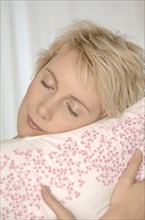 Blonde woman hugging a cushion with her eyes closed