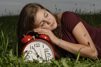 Teenage girl lying on the grass and sleeping on an oversized alarm clock