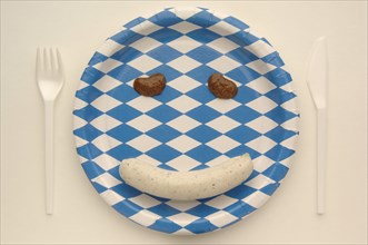 Weisswurst veal sausage making a face with mustard on a paper plate with the Bavarian diamond pattern