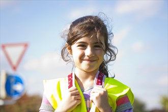 Girl wearing a safety vest in front of a road sign