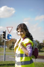 Girl with a school bag wearing a safety vest in front of a road sign