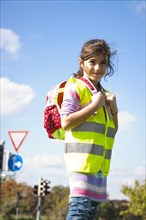 Girl with a school bag wearing a safety vest in front of a road sign