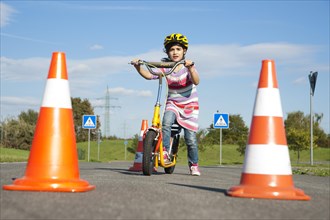 Girl practicing to ride slalom on a scooter at a traffic awareness course