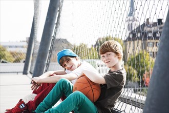 Two cool boys sitting with a basketball on a playground