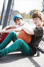 Two cool boys sitting with a basketball on a playground