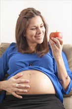 Pregnant woman holding hand on her stomach and eating an apple