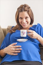 Smiling pregnant woman drinking coffee