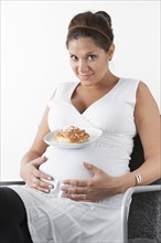 Pregnant woman holding hands on her stomach and resting a plate with a sweet bun on her belly