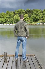 Man standing on jetty by a lake and looking at rainclouds