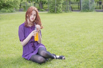 Young woman sitting in a park with a bottle of orange soda