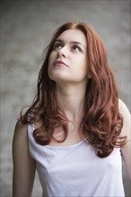 Pensive young woman with red hair looking up