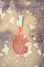 Plastic toy tennis racket in dirty puddle