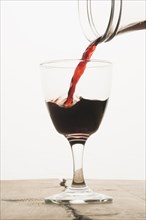 A glass of red wine being filled from a carafe